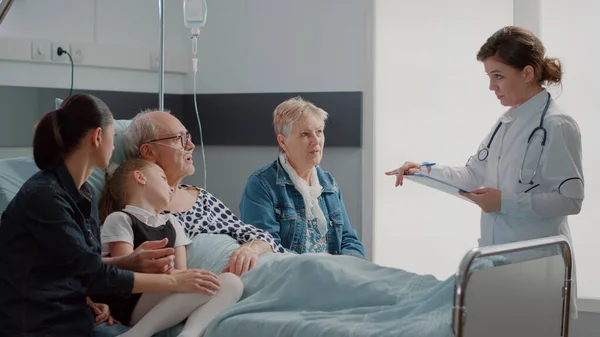 Médico haciendo visita de chequeo con la familia visitando pensionista enfermo en la sala de hospital —  Fotos de Stock