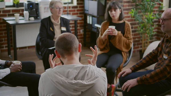 Man with anger management issues talking to people and counselor at aa group meeting