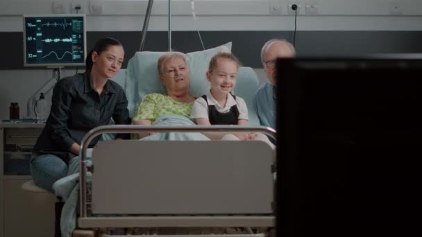 Посетители смотрят телевизор со старшим пациентом в больничном отделении — стоковое видео