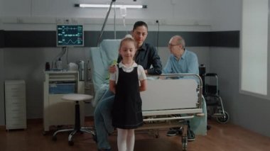 Portrait of child and mother visiting old patient in hospital ward bed