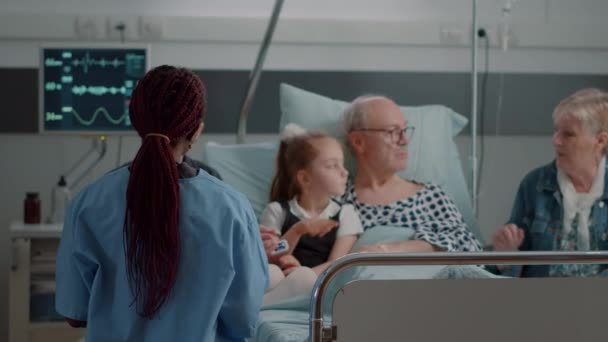 Закрытие медсестры, объясняющей диагноз пожилому человеку и его семье во время визита — стоковое видео