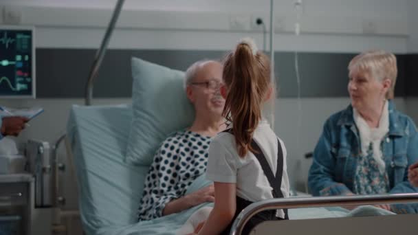 Zbliżenie z małą dziewczynką odwiedzając emeryta z chorobą w szpitalu oddział łóżko — Wideo stockowe