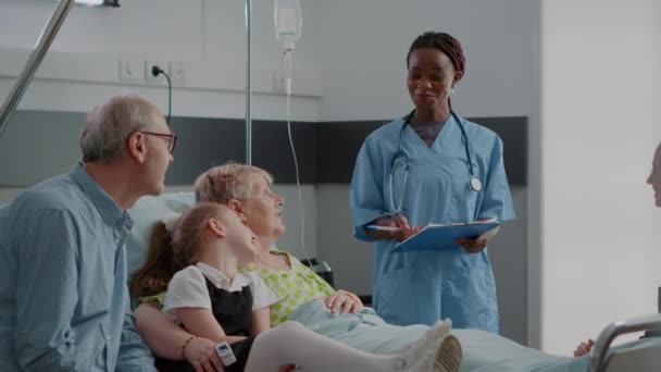 Zbliżenie asystent medyczny wyjaśniający choroby do pacjenta i rodziny w trakcie wizyty — Wideo stockowe