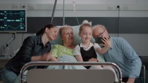 Семья фотографируется со старым пациентом в палате больницы — стоковое видео