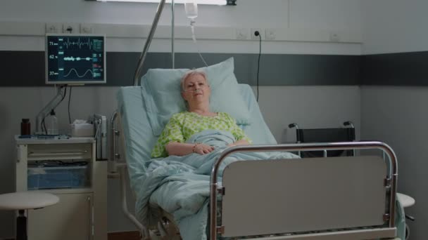 Portrait of old woman sitting in hospital ward bed to cure disease — Stockvideo