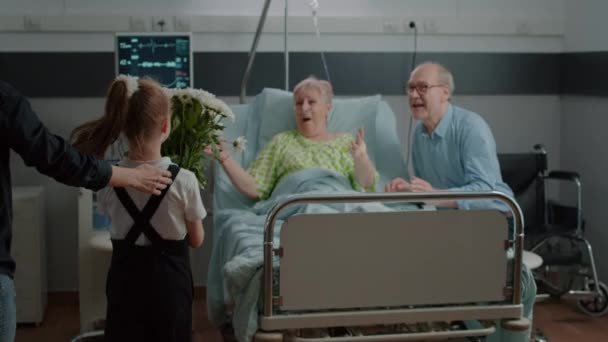 Hastane koğuşundaki yaşlı hastaya sarılıp çiçek vermek için koşan küçük kız. — Stok video