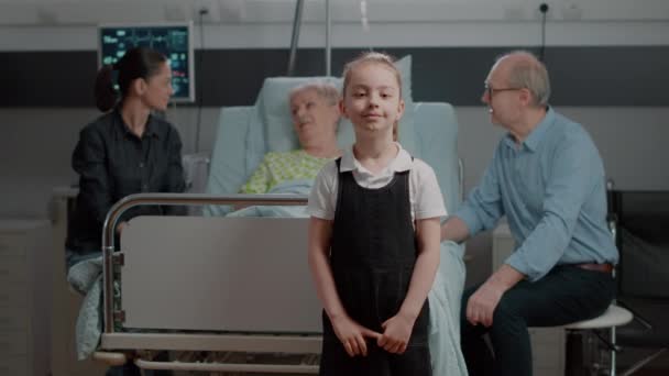 Egy kislány portréja, aki a kórházi kórteremben ül a családi látogatáson. — Stock videók