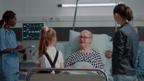 Aged patient talking to little girl in hospital ward bed — Stock video