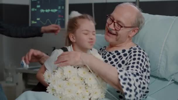 Zbliżenie się z mała dziewczynka przynosząc kwiaty do dziadka w szpitalu oddział łóżko — Wideo stockowe