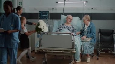 Senior man receiving visit from mother and little girl in hospital ward