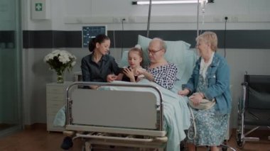 Old man and niece browsing internet on smartphone in hospital ward bed