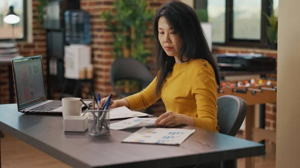 Asijská žena analyzuje prodejní grafy na souborech a notebooku — Stock fotografie