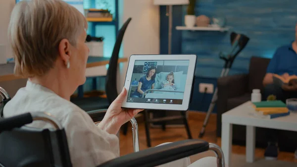 Oudere persoon in een rolstoel met tablet met online videogesprek — Stockfoto