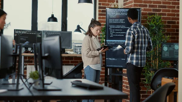 Software developer holding digital tablet analyzing code on wall screen tv explaining errors to coworker programer — Stok fotoğraf