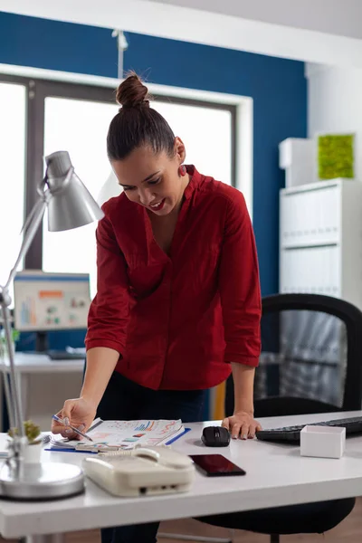 Businesswoman standing near desk in startup office looking at charts. — Stockfoto