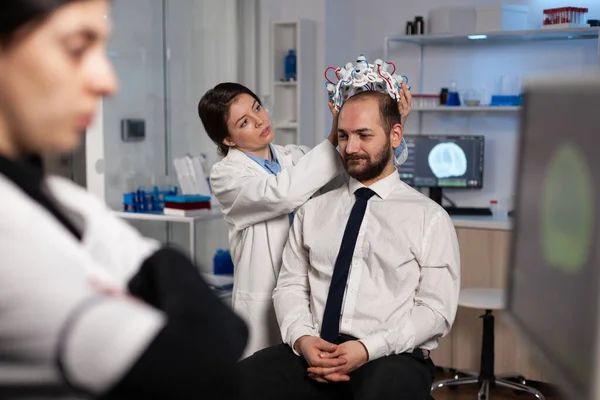 Specialist neurologist woman adjusting eeg headset analyzing brain activity of man patient — Foto de Stock
