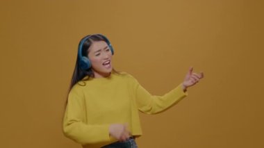 Asian woman playing air guitar and wearing headphones