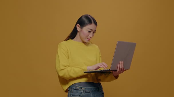 Asian woman using laptop in front of camera over yellow background — Stock Video