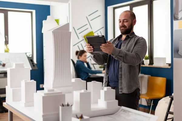 Skäggig professionell arkitekt tittar på surfplatta framför vit skumplast byggnad modell — Stockfoto