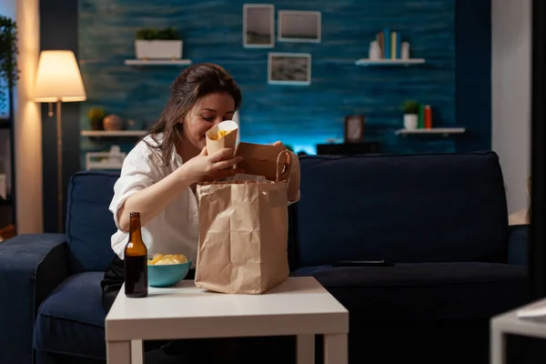 거실에 있는 여자가 쇼파 저녁 식사를 준비하면서 감자튀김 과 맛있는 햄버거를 꺼내는 모습 — 스톡 사진