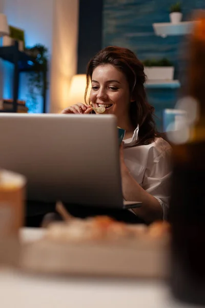 Крупним планом портрет усміхненої жінки, що дивиться онлайн телешоу на портативному комп'ютері, що має смачну закуску — стокове фото