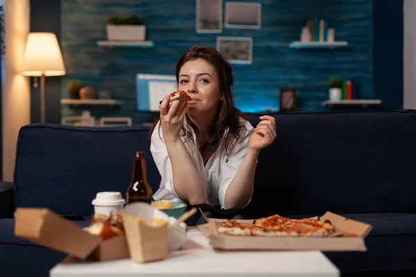 Жінка після офісної роботи виймає шматочок гарячої доставки піци під час перегляду телевізора — стокове фото