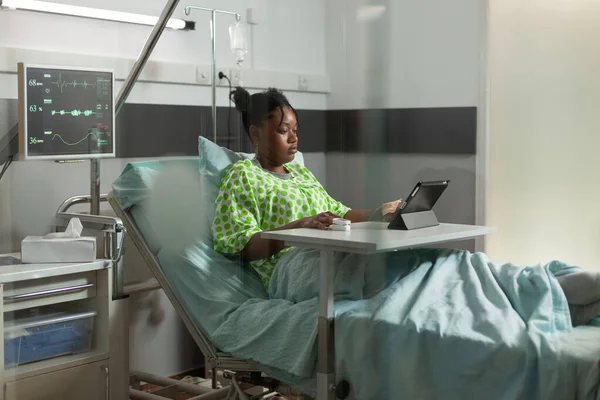 Afro-Amerikalı genç hasta, tıbbi ameliyattan sonra iyileşme sürecinde yatıp internette çizgi film seyrediyor. — Stok fotoğraf