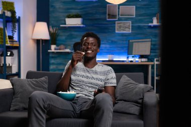 Genç adam kanepede oturmuş televizyon seyrediyor.