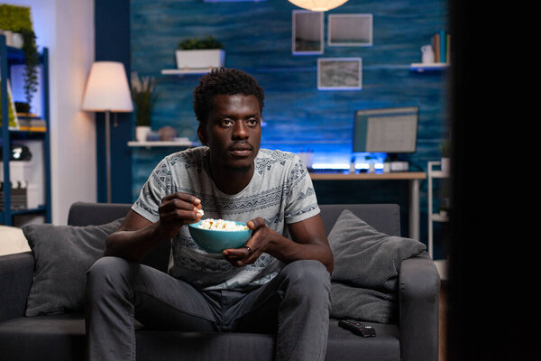Young adult watching television eating popcorn snacks while waiting for soccer goal
