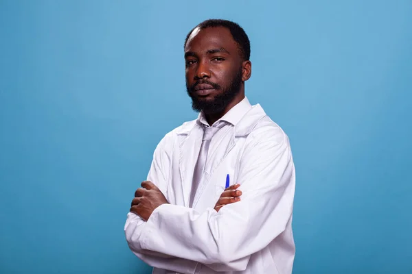 Retrato de médico confiado en uniforme de laboratorio posando con los brazos cruzados sobre fondo azul —  Fotos de Stock