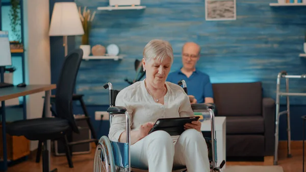 Mulher idosa usando tablet digital enquanto ela se senta em cadeira de rodas — Fotografia de Stock