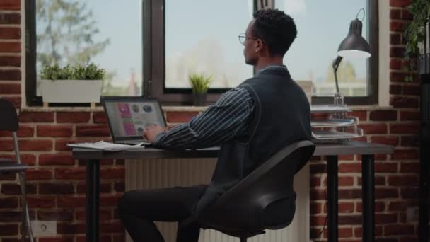 Африканский американский рабочий планирует коммерческий отчет на ноутбуке — стоковое видео