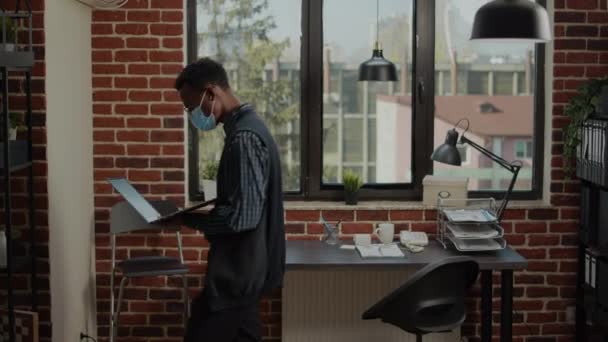Niecierpliwy pracownik spacerujący po biurze z laptopem w ręku — Wideo stockowe