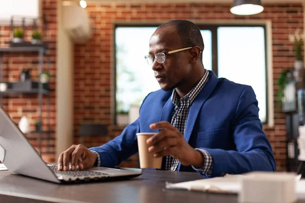 Persona afroamericana que trabaja en proyecto de negocios con computadora portátil y taza de café — Foto de Stock