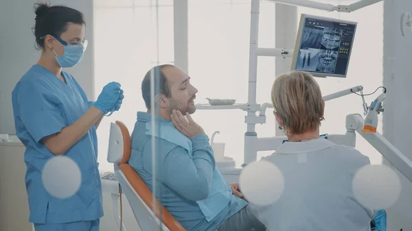 Dentysta pokazujący pacjentowi radiografię zębów na krześle dentystycznym — Zdjęcie stockowe