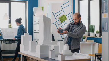 Mühendis, mimari ofisindeki model ve düzen üzerinde çalışmak için akıllı telefonu kullanıyor.