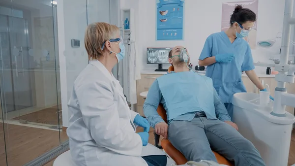 Ассистент стоматолога надевает кислородную маску на лицо пациента — стоковое фото