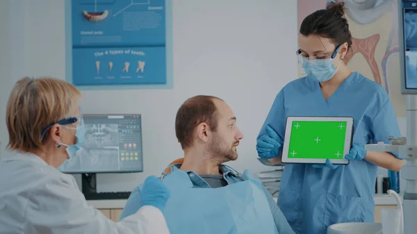 Команда пациентов и стоматологов рассматривает планшет с зеленым экраном — стоковое фото