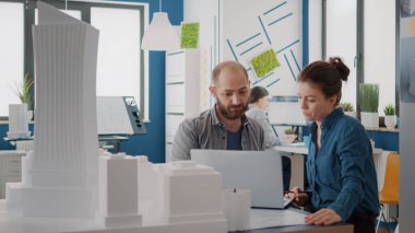 Bina modelini ve tasarım planlarını analiz etmek için laptopta çalışan meslektaşlar