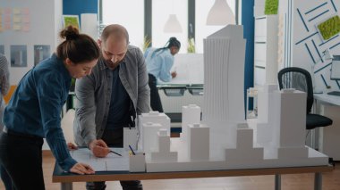 Mimarlık ve inşa modeli üzerinde çalışmak için maketi ve planları analiz eden iş arkadaşları.