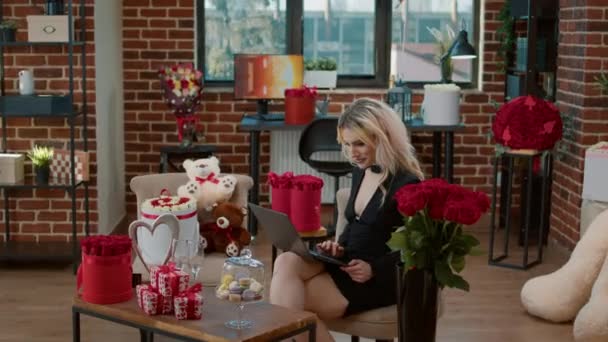 Mosolygó gyönyörű nő a szent Valentin napon tartja laptop a szobában tele vörös rózsákkal óriás plüssmackó — Stock videók