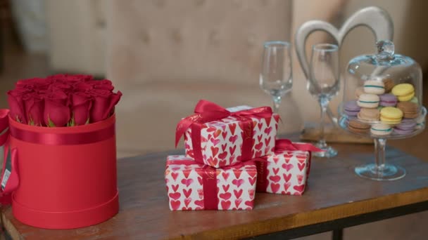 Κουτιά δώρων για την ημέρα του Αγίου Βαλεντίνου με κόκκινες καρδιές χαρτί περιτυλίγματος στο τραπεζάκι δίπλα σε πολυτελή κόκκινα τριαντάφυλλα μπουκέτο — Αρχείο Βίντεο