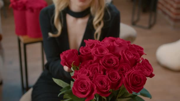 Nahaufnahme einer blonden attraktiven Frau, die einen Strauß mit roten Rosen riecht — Stockvideo