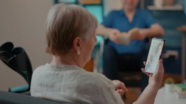 Koltuk değnekleriyle akıllı telefondan video izlemenin keyfini çıkaran yaşlı bir kadın.