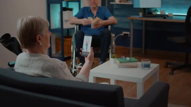 У віці жінка використовує відеодзвінок, щоб поговорити з лікарем про лікування — стокове відео
