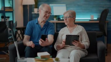 Modern çift evde akıllı telefon ve dijital tablet kullanıyor.