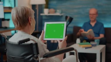 Tekerlekli sandalyedeki yetişkin elinde yeşil ekranlı dijital tablet