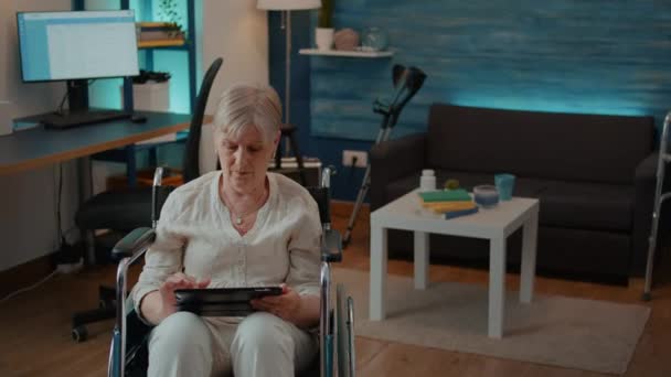 Gepensioneerde die digitale tablet gebruikt en in een rolstoel zit — Stockvideo