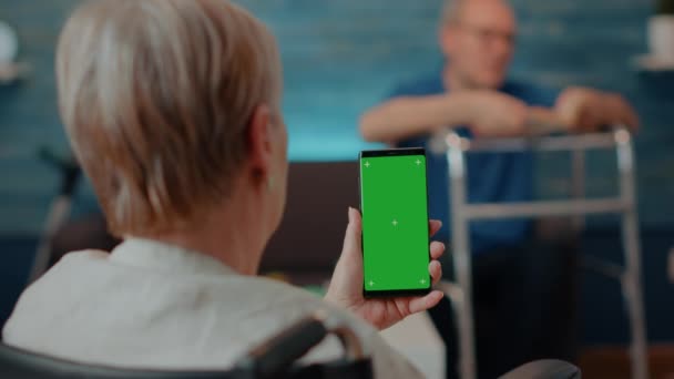 Старшая женщина в инвалидной коляске держит смартфон с зеленым экраном — стоковое видео