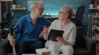 Yaşlı çift oturma odasındaki tablet ekrana bakıyor.